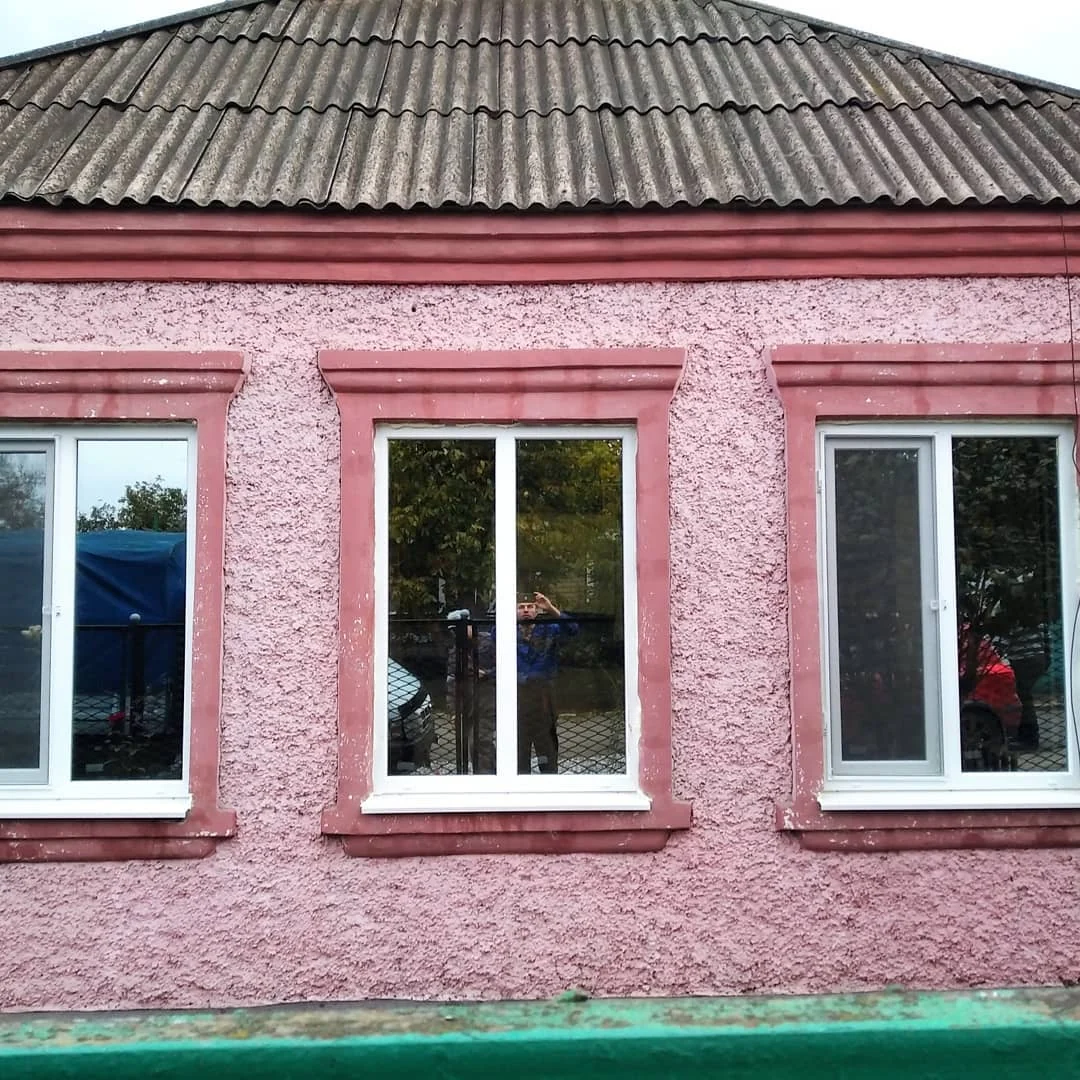 Білі вікна на рожевому фасаді з обрамленням прорізів