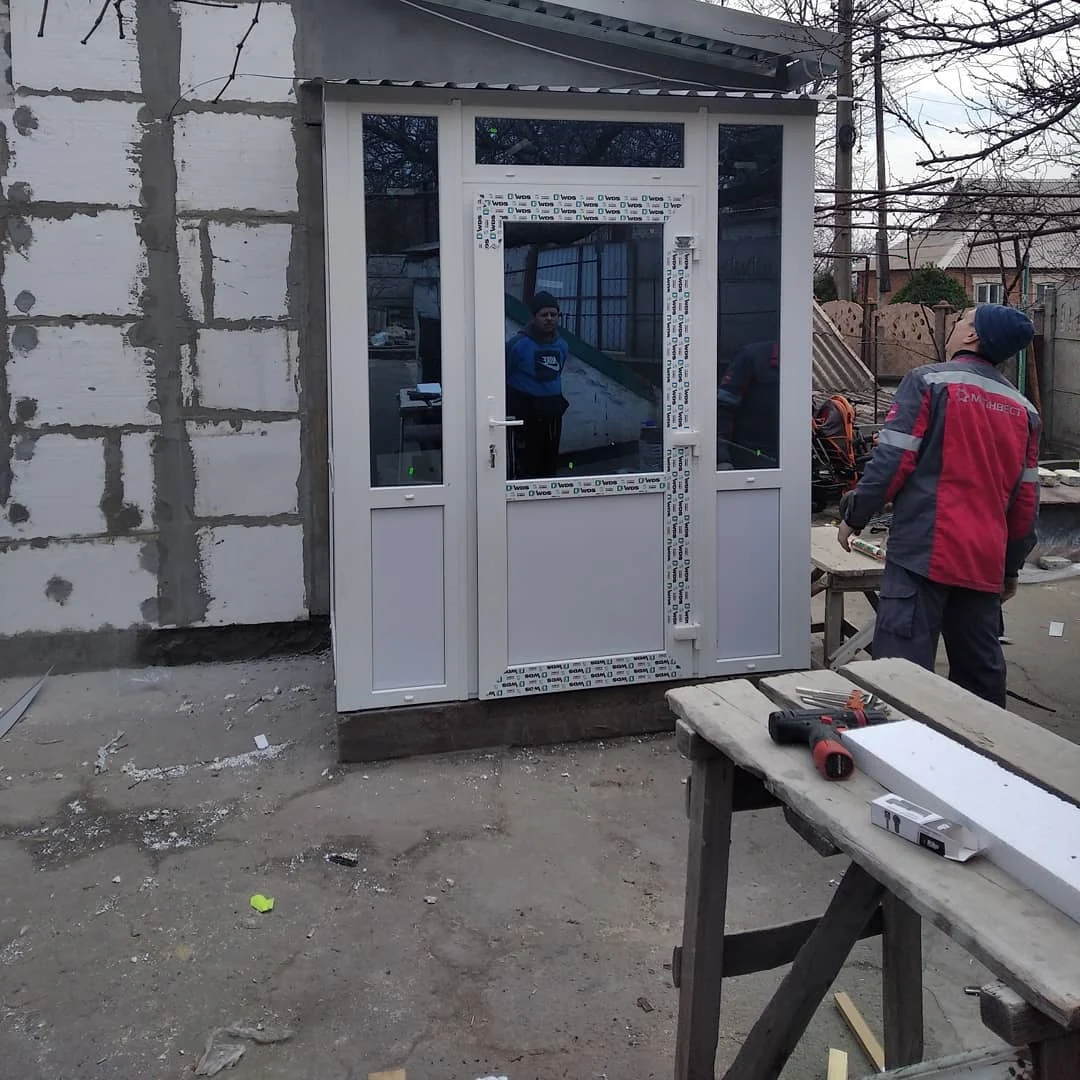 Білий вхідний блок зі склінням і бічними секціями під час монтажу